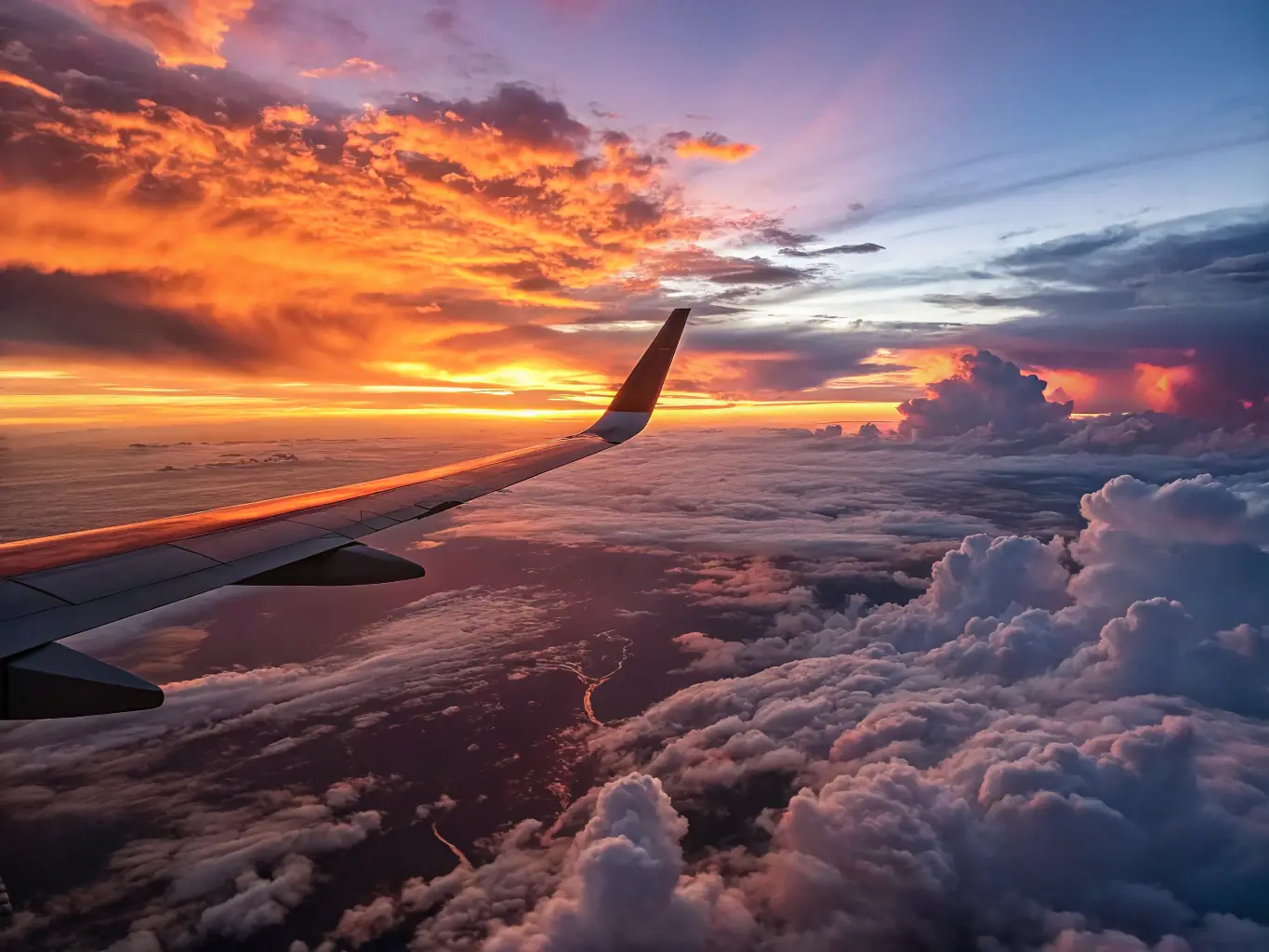 A scenic image of a commercial airplane soaring above clouds at sunset, with a panoramic view of the sky, symbolizing global travel opportunities and adventure.
